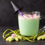 Brebaje de la bruja de chocolate blanco caliente con nubes rosas en una taza de cristal