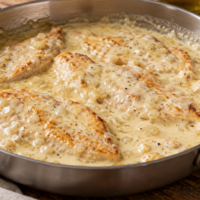 Filetes de pollo en una sartén con salsa de queso semicurado